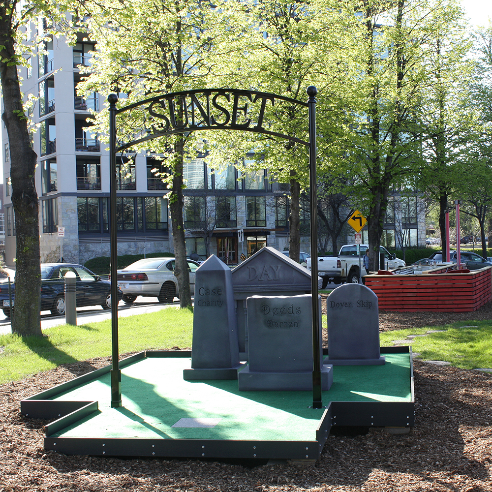 Mini-golf hole design to look like a cemetery, with steel gate, fiberglass tombstones, and artificial turf.