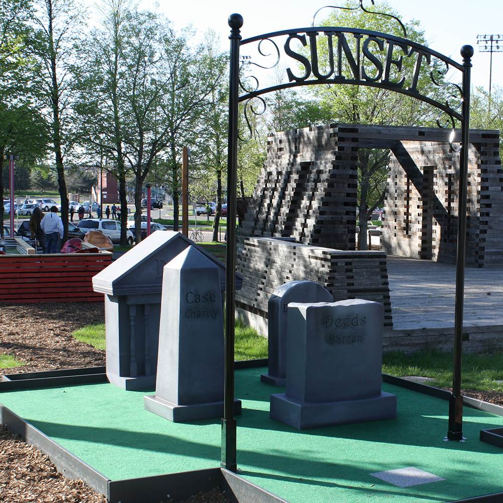 Mini-golf hole design to look like a cemetery, with steel gate, fiberglass tombstones, and artificial turf.